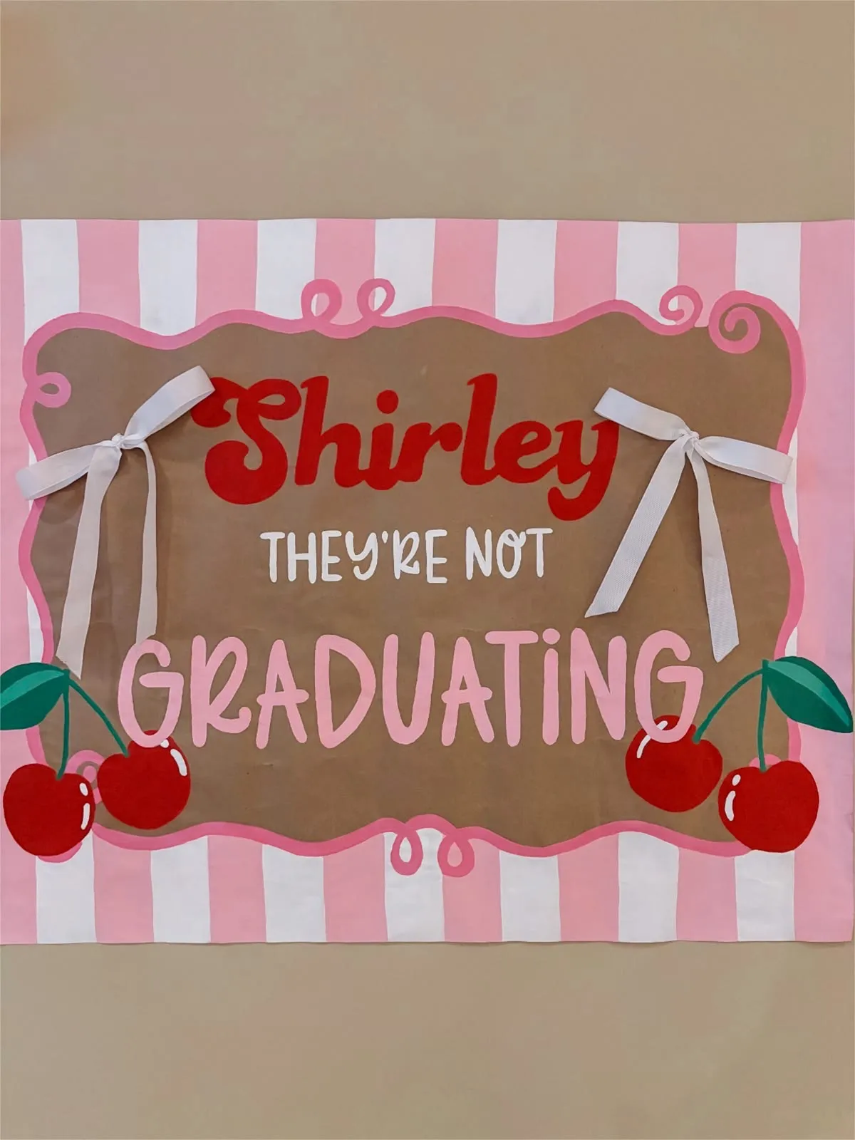 Hand-painted graduation banner on kraft paper with pink stripes, cherries, and white bows